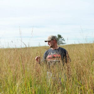 A man standing in tall grass with Bedding in a Bag - Per Acre.