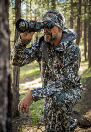 A man looking through binoculars in the woods.