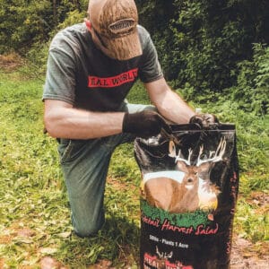 A man kneeling down next to a bag of deer food.